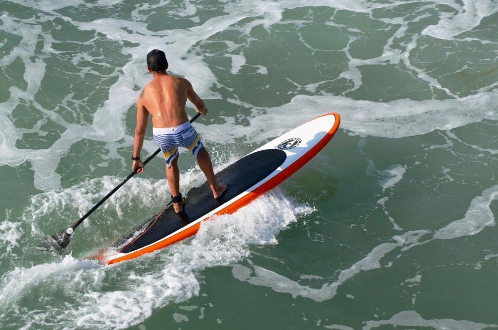 SUP surfing man. Paddleboarding wave paddling surfer
